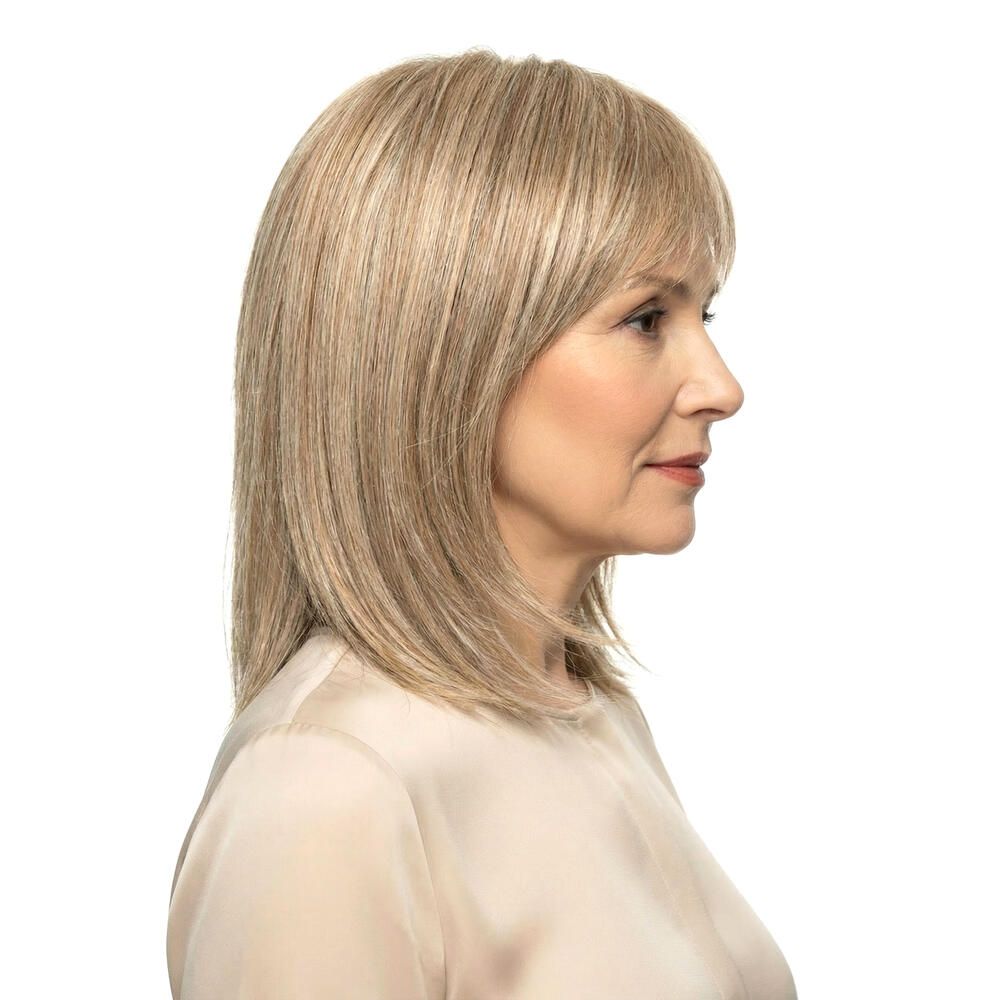 Blond gefärbte Perücke mit Pony. Mittellange, gestufte Haare. Frau mit hellem Oberteil. Seitenansicht.