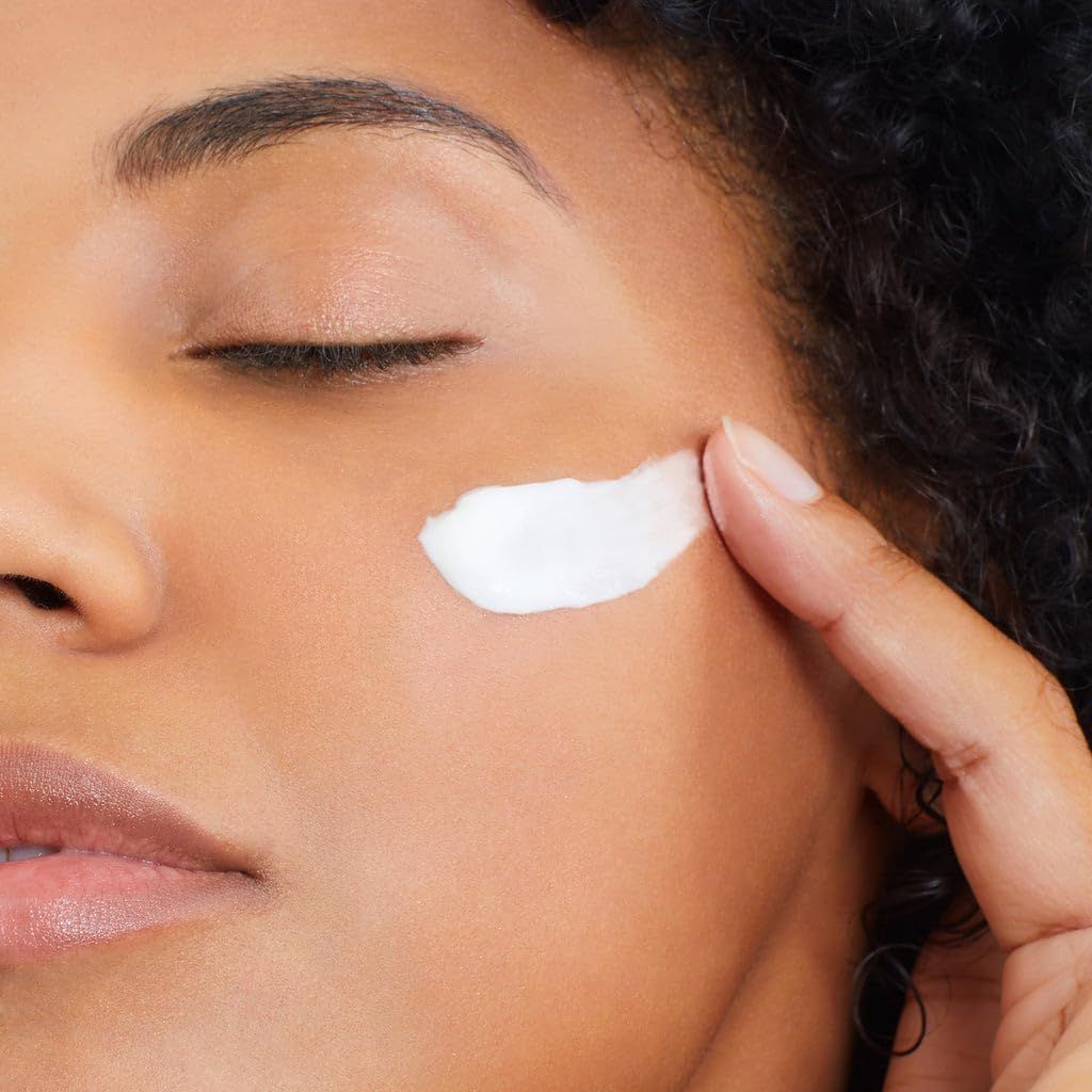 Nahaufnahme einer Frau, die Creme auf ihre Wange aufträgt. Weiße Creme sichtbar.