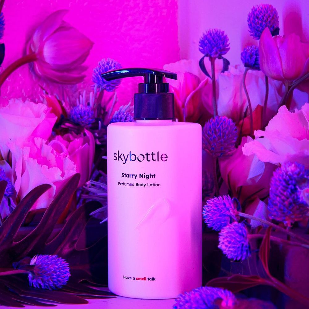 Weiße Flasche mit schwarzem Pumpkopf, umgeben von lila Blumen. Aufschrift: skybottle, Starry Night, Perfumed Body Lotion.