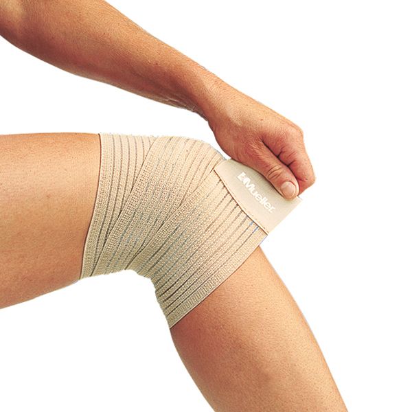 Beige elastische Bandage am Knie. Das Produkt wird mit einer Hand angebracht. Das Logo von Mueller ist sichtbar.