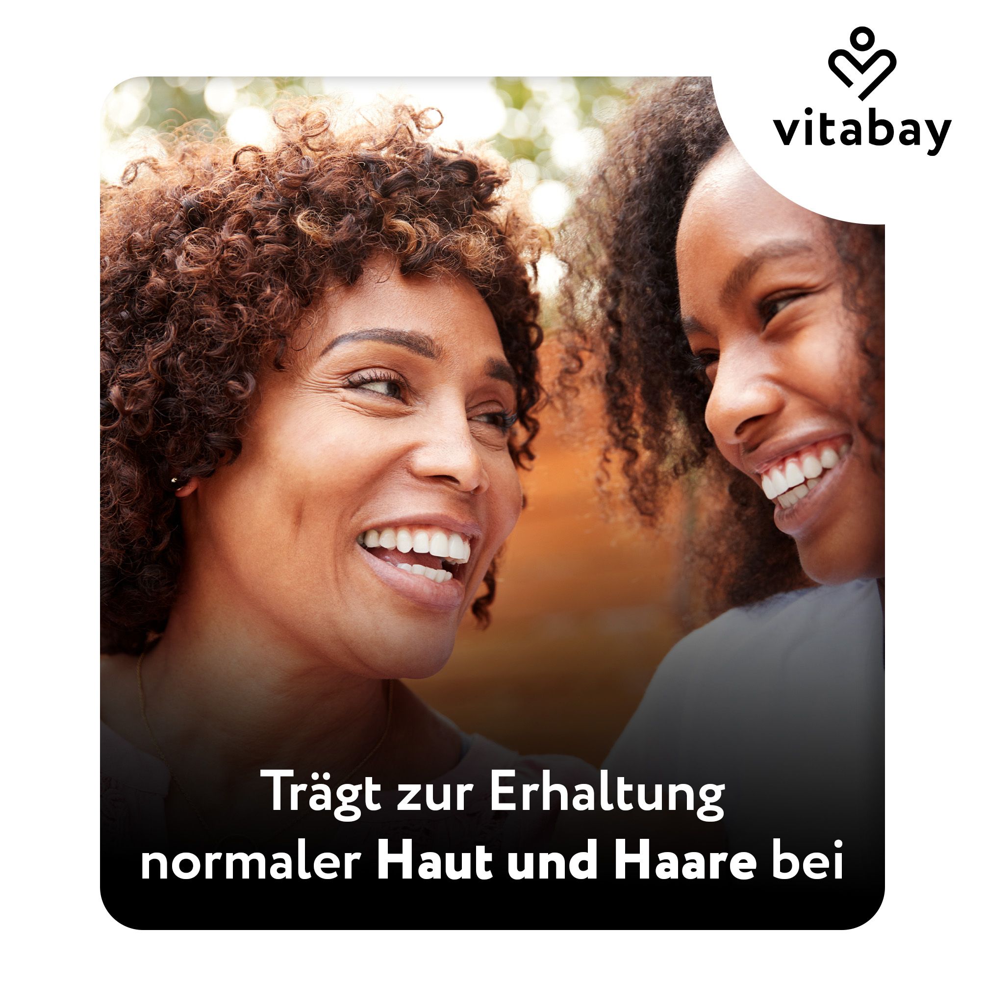 Zwei Frauen lächeln. Vitabay Logo. Text: Trägt zur Erhaltung normaler Haut und Haare bei.