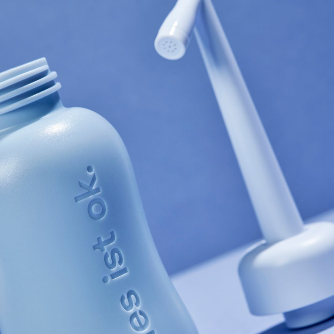 Nahaufnahme einer Intimdusche und Flasche in Hellblau. Schriftzug "alles ist ok."