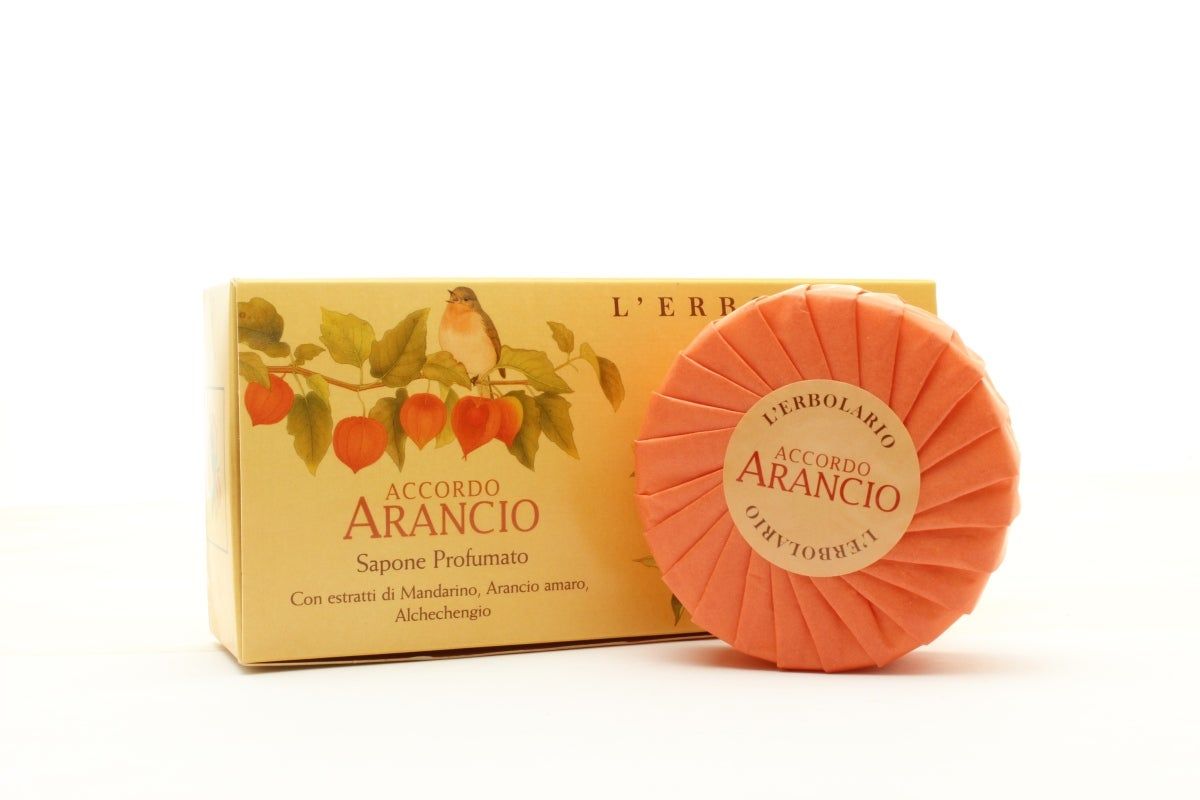 Orangefarbene Seife und Schachtel. Aufschrift: ACCORDO ARANCIO. Verpackung mit Illustrationen von Blättern, Vogel und Früchten.