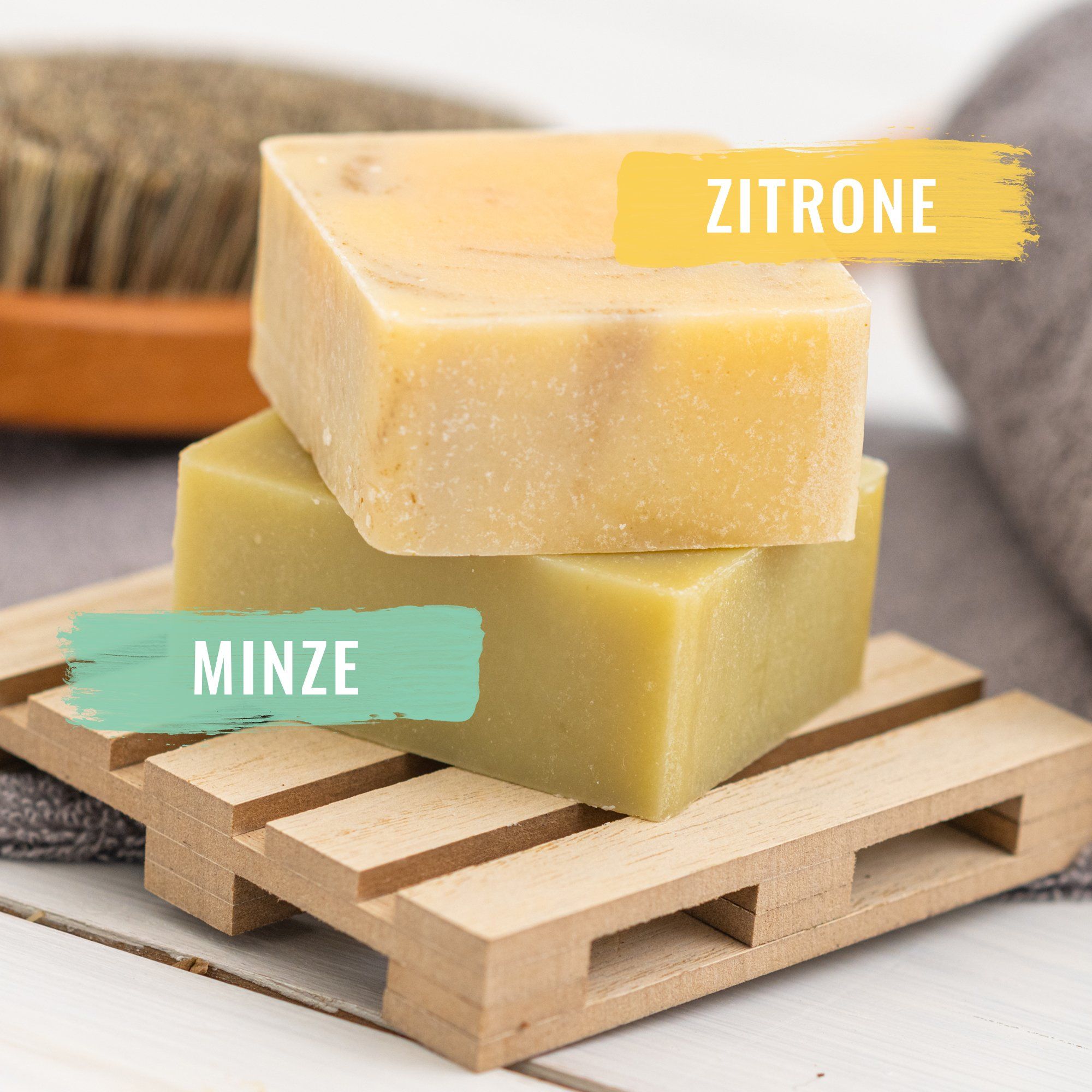 Zwei Seifenstücke auf Holzpalette. Aufschrift: Zitrone und Minze.