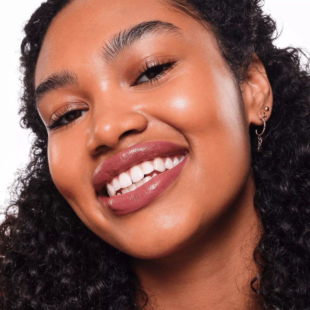 Nahaufnahme eines lächelnden Gesichts mit Lippenstift. Lippen in Rosé-Ton geschminkt. Haut mit Glanz.