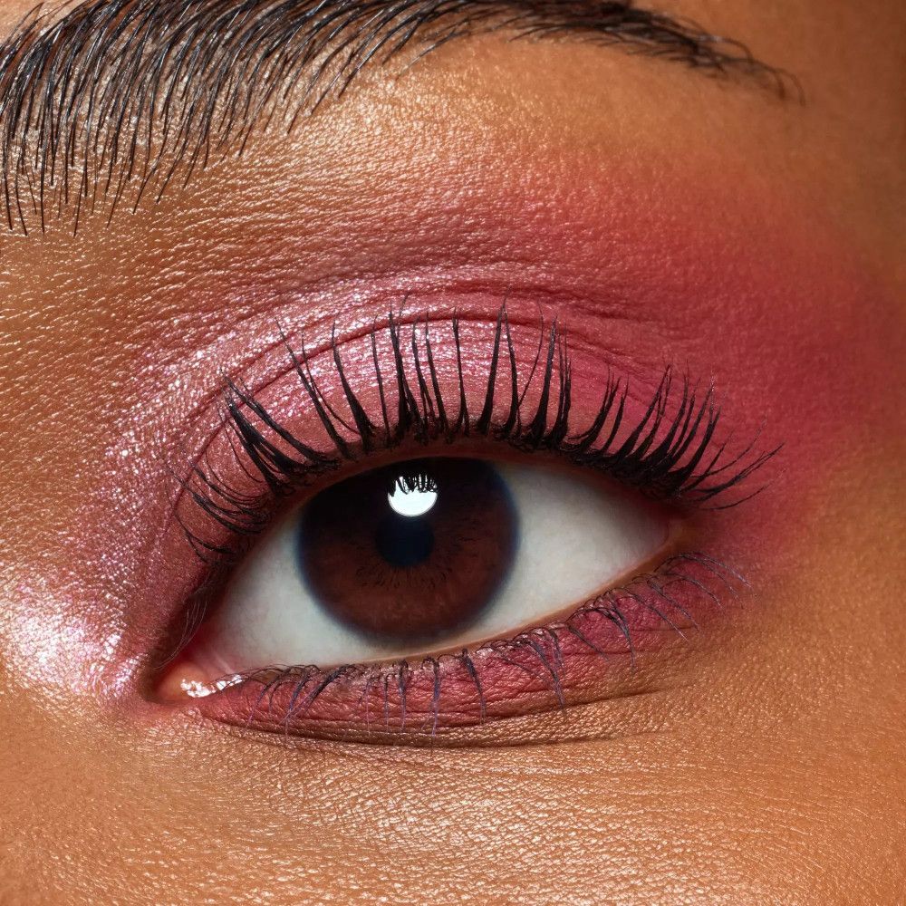 Nahaufnahme eines Auges mit rosa Lidschatten. Wimpern sind getuscht. Braune Iris, helle Haut.