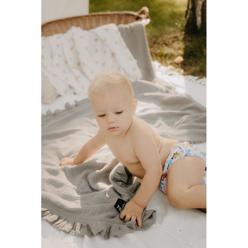 Baby sitzt auf einer Decke. Trägt Schwimmwindel. Graue Decke und Kissen im Hintergrund. Ein graues Tuch mit Label.