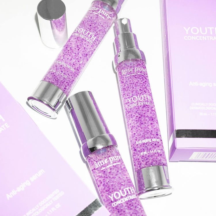 Mehrere Serumflaschen mit silbernen Deckeln. Aufschrift: âme pure, Youth Concentrate, Anti-aging serum. Lila Inhalt.