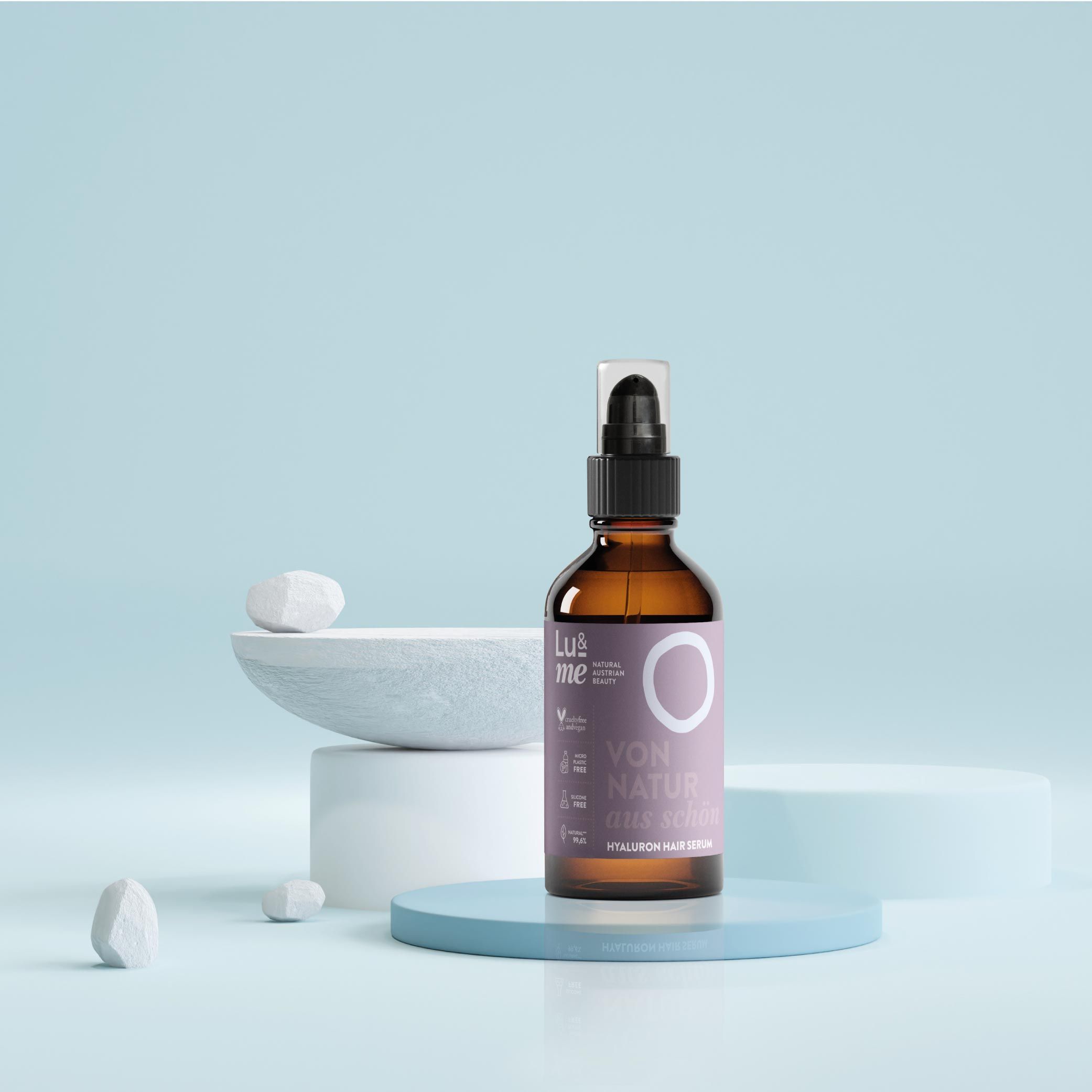 Braune Glasflasche mit schwarzem Sprühkopf auf blauem Podest. Etikett mit Logo und Text. Steine und Schale im Hintergrund.