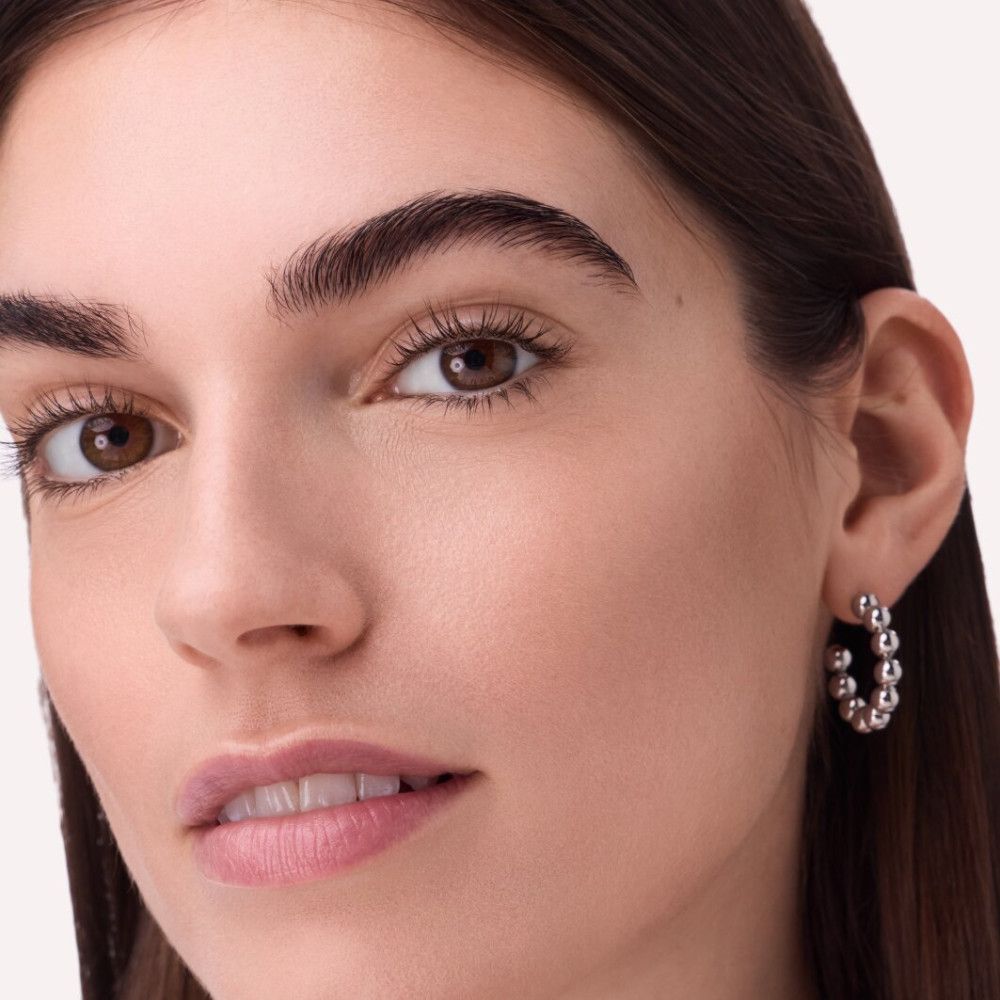 Nahaufnahme einer Frau mit Make-up. Fokus auf Gesicht. Deutliche Augenbrauen, Lippenstift, Ohrringe.