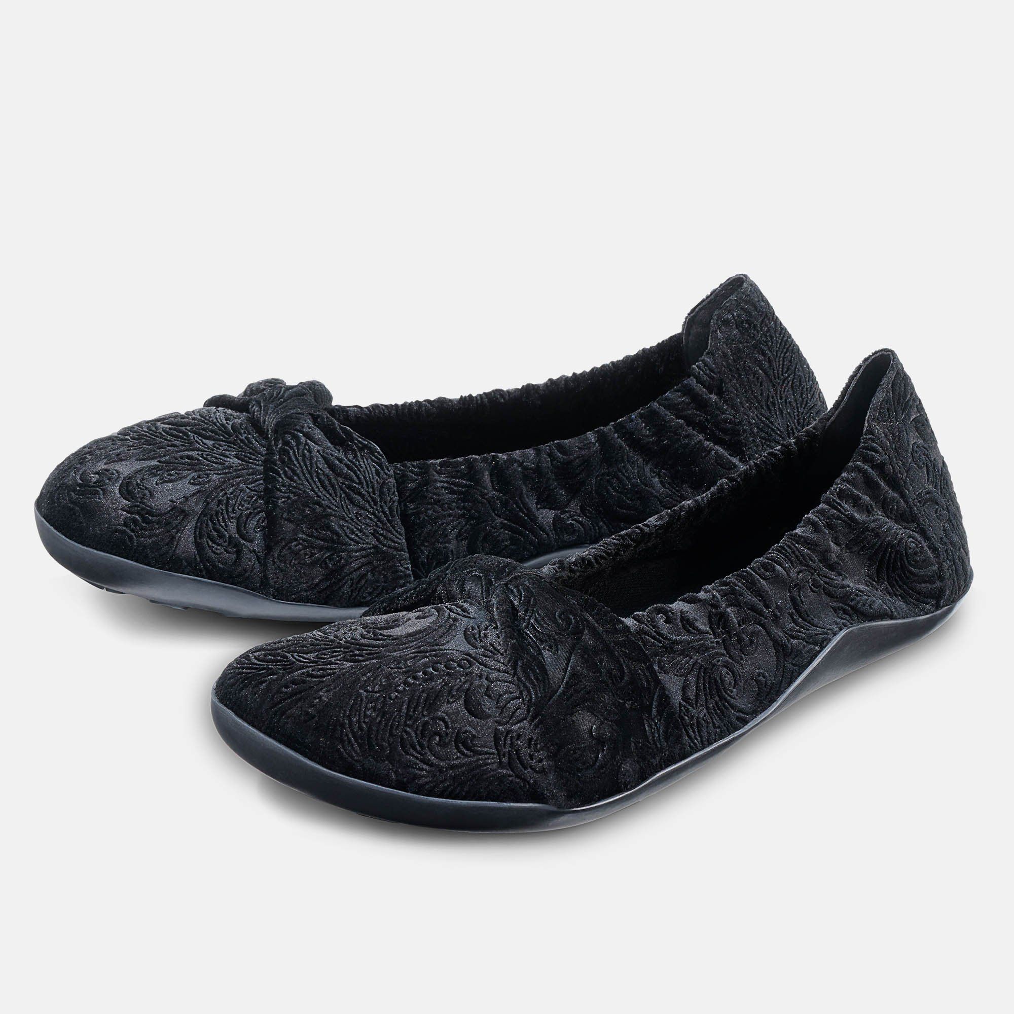 Schwarze Ballerinas mit floralem Muster. Zwei Schuhe nebeneinander, mit Schleife und elastischem Bund. Weite: breit.