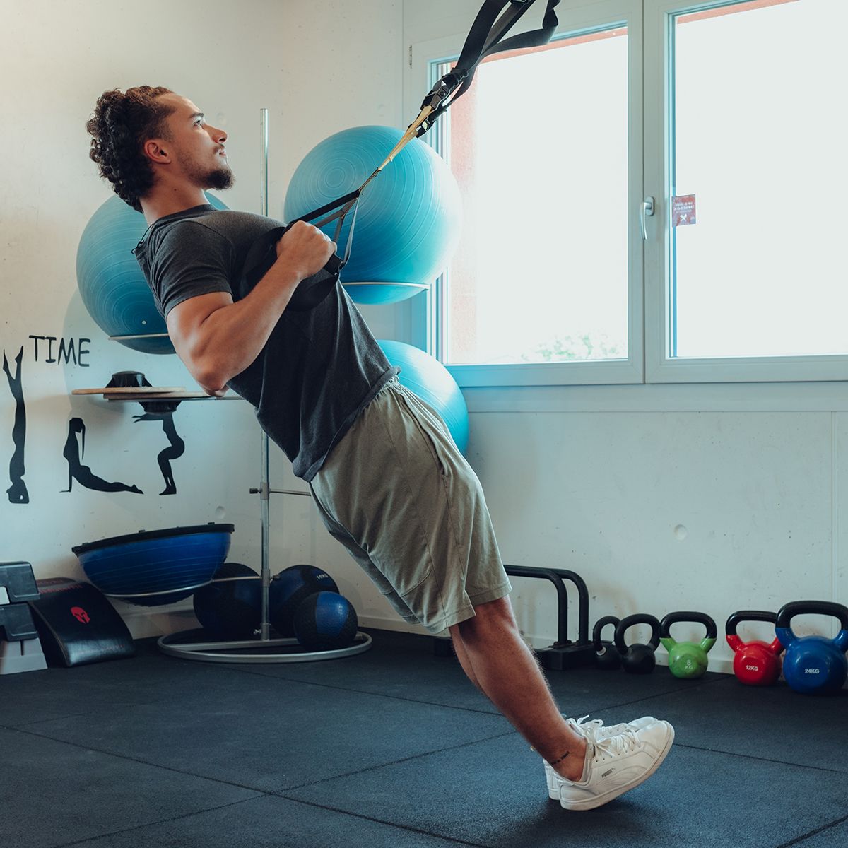 Mann trainiert mit gelb-schwarzen Aufhängegurten in einem Fitnessstudio. Hält sich an Griffen fest.