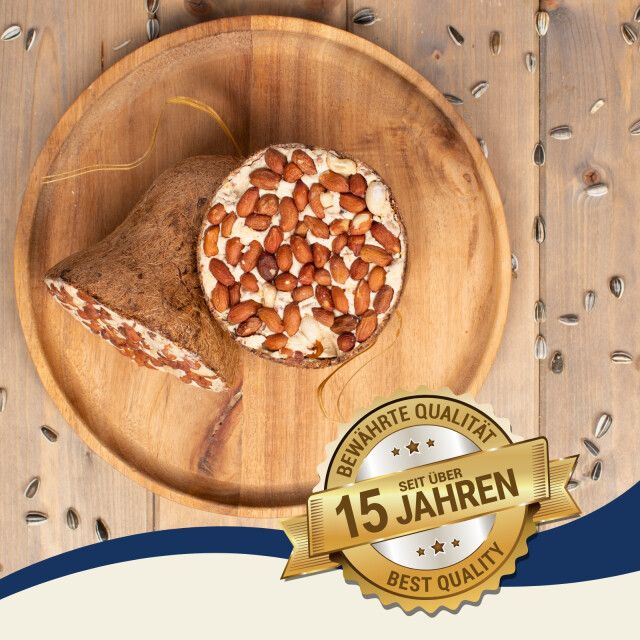 Vogelfutter in Form eines halbierten Kokosnussprodukts und einer Scheibe auf einem Holztablett. Qualitätsmarke: Seit über 15 Jahren.