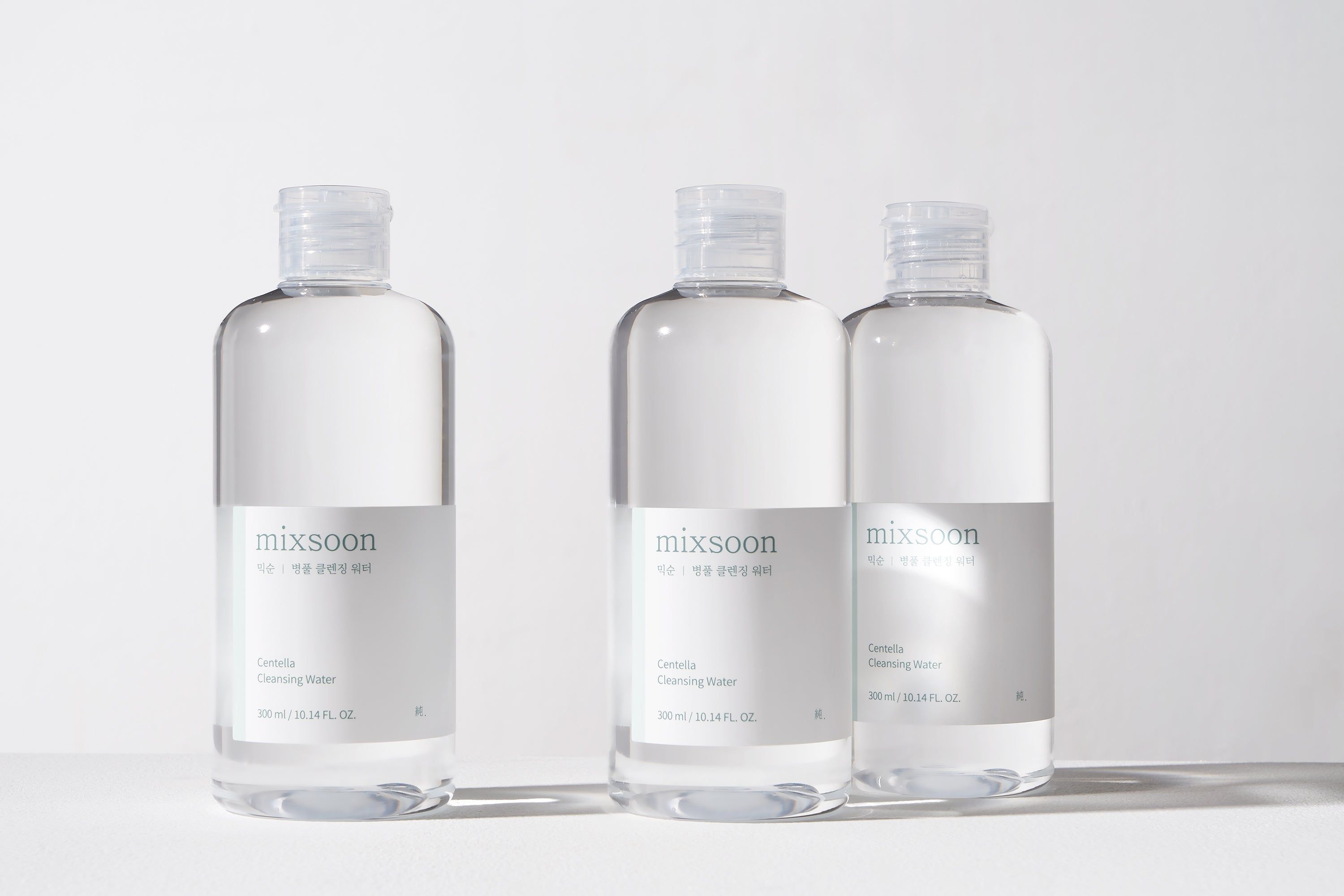 Drei Flaschen mit weißem Etikett. Aufschrift: mixsoon Centella Cleansing Water. Produkt auf hellem Hintergrund.