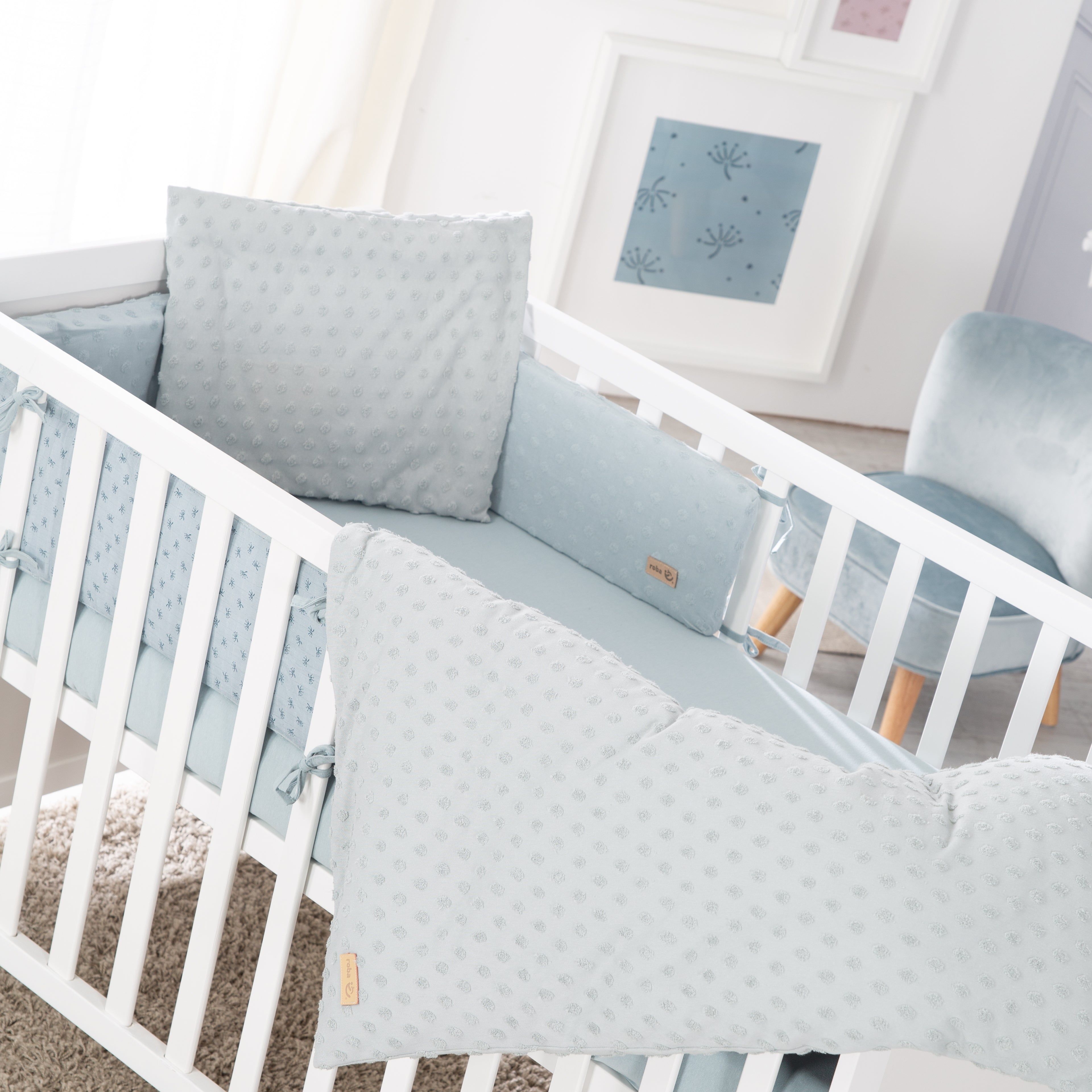 Hellblaues Babybett-Set mit Kissen, Nestchen und Bettwäsche. Weiße Holzstruktur. Aufdruck mit kleinen Punkten.