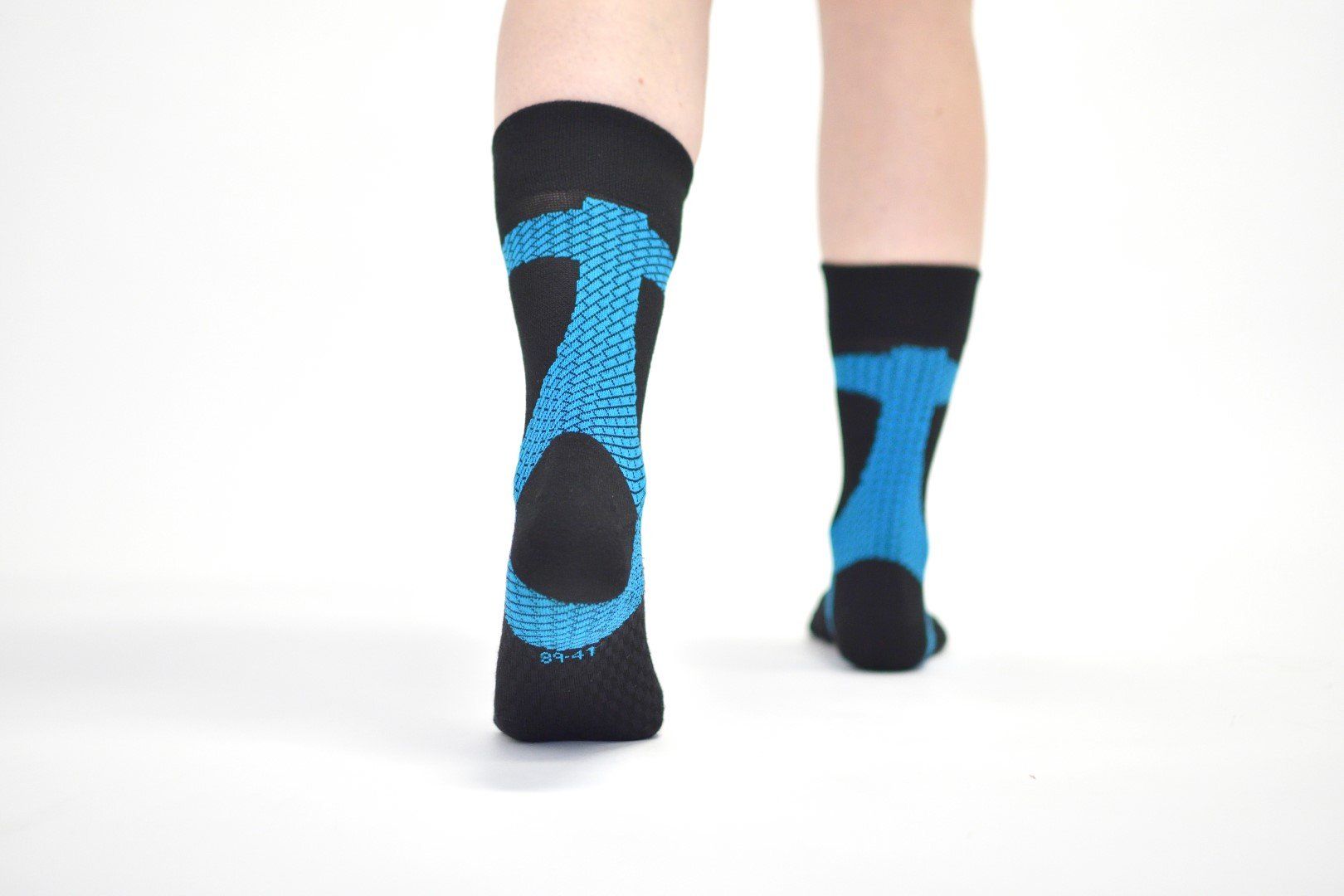Due piedi indossano calzini neri Enforma Achilles Support con design blu. I calzini coprono i piedi e le caviglie. Lo sfondo è bianco.
