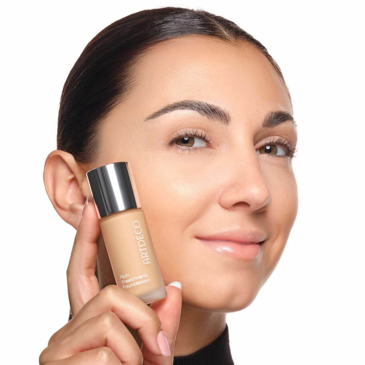 Frau hält eine Artdeco Rich Treatment Foundation Flasche. Sie lächelt.