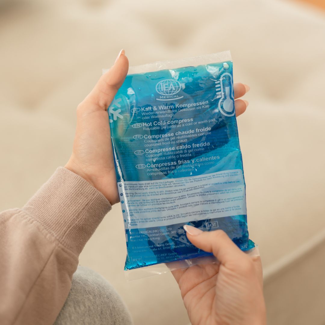 Mani che tengono una compressa caldo-fredda blu. Stampato: IEA Medical, Hot Cold compress.