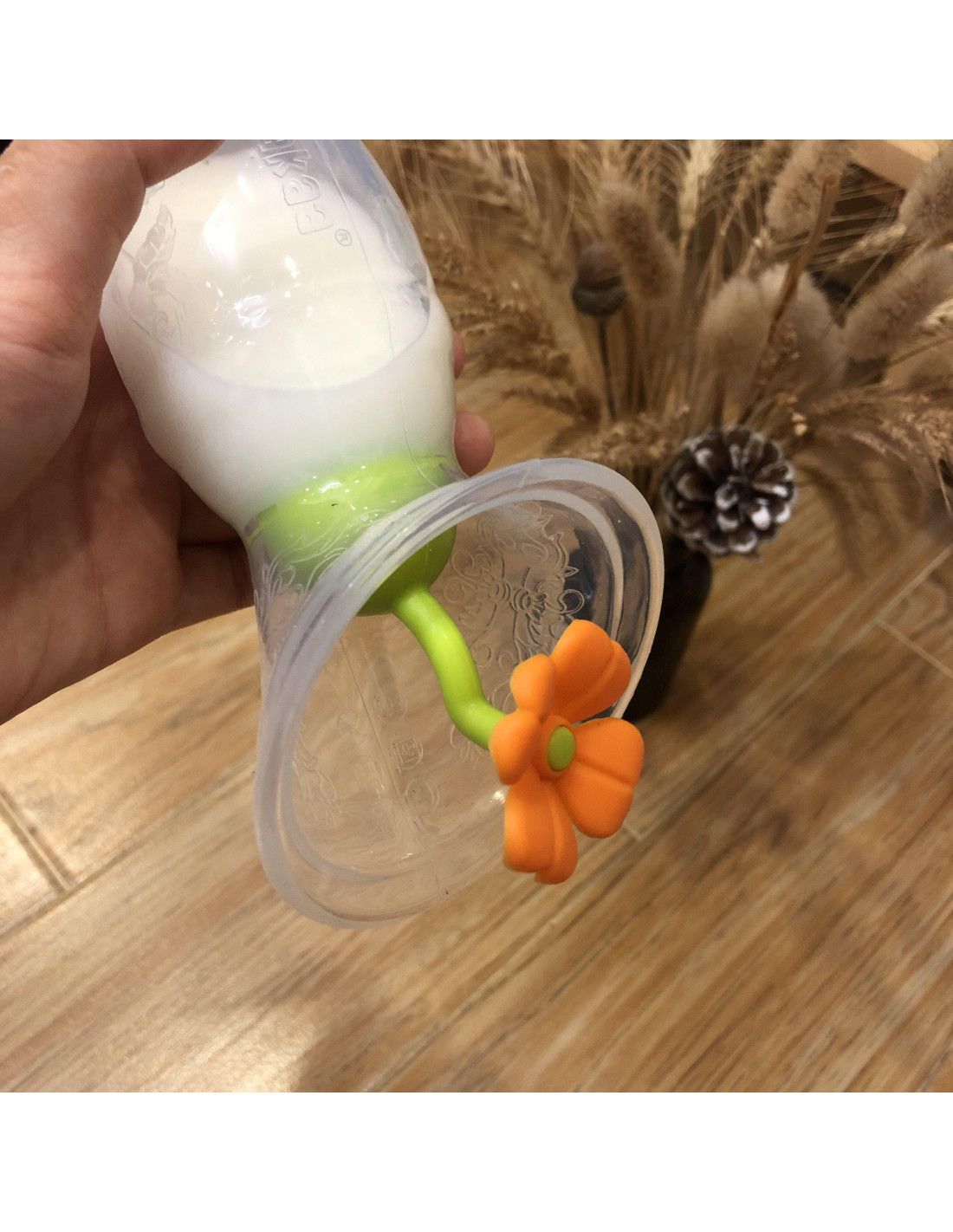 Blumenförmiger Verschluss an einer Milchpumpe. Orangefarbene Blüte, grüner Stiel, transparente Pumpe, Hand hält Pumpe.