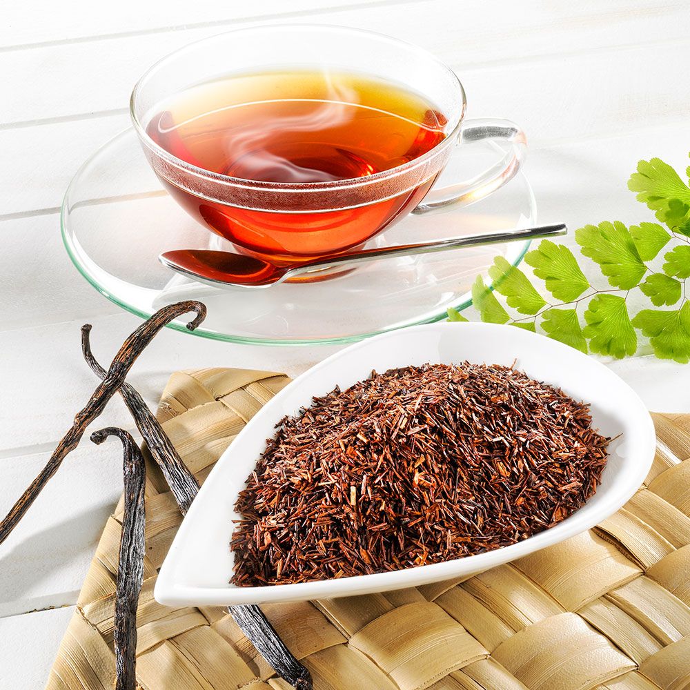 Glas-Teetasse mit Untertasse und Löffel. Daneben eine Schale mit losem Tee und Vanilleschoten. Auf hellem Untergrund.