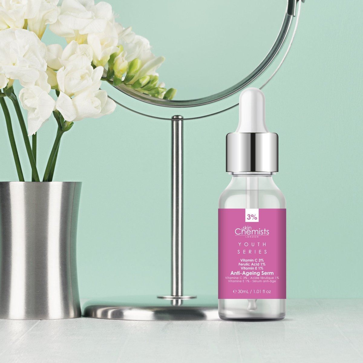 SkinChemists Anti-Aging Serum neben einem Spiegel und Blumenarrangement auf einem Tisch.