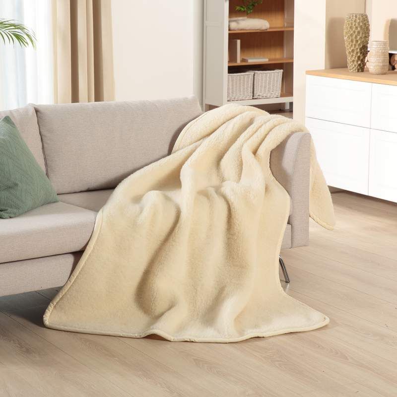 Beige Schurwolldecke auf Sofa. Weiche Textur, rechteckige Form. Liegt über der Sofalehne.