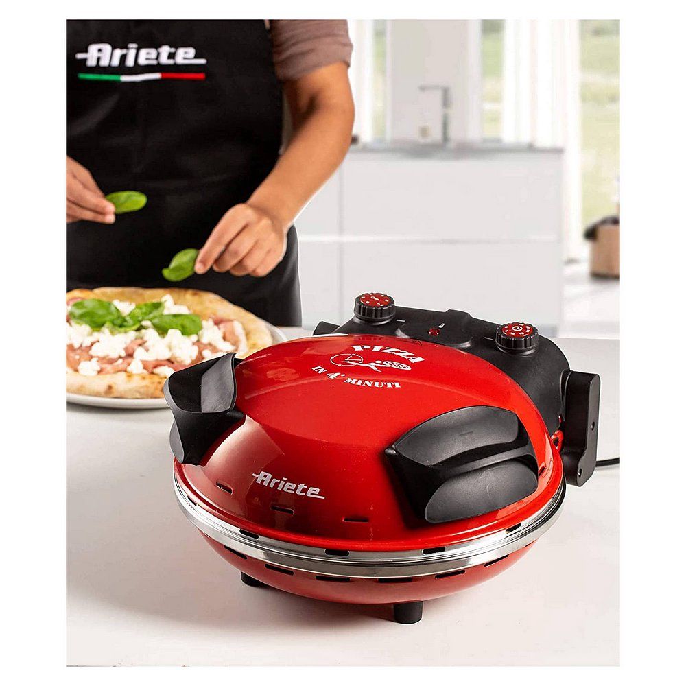 Roter Ariete Pizzaofen auf einer Arbeitsplatte, daneben eine Person, die Pizza belegt.