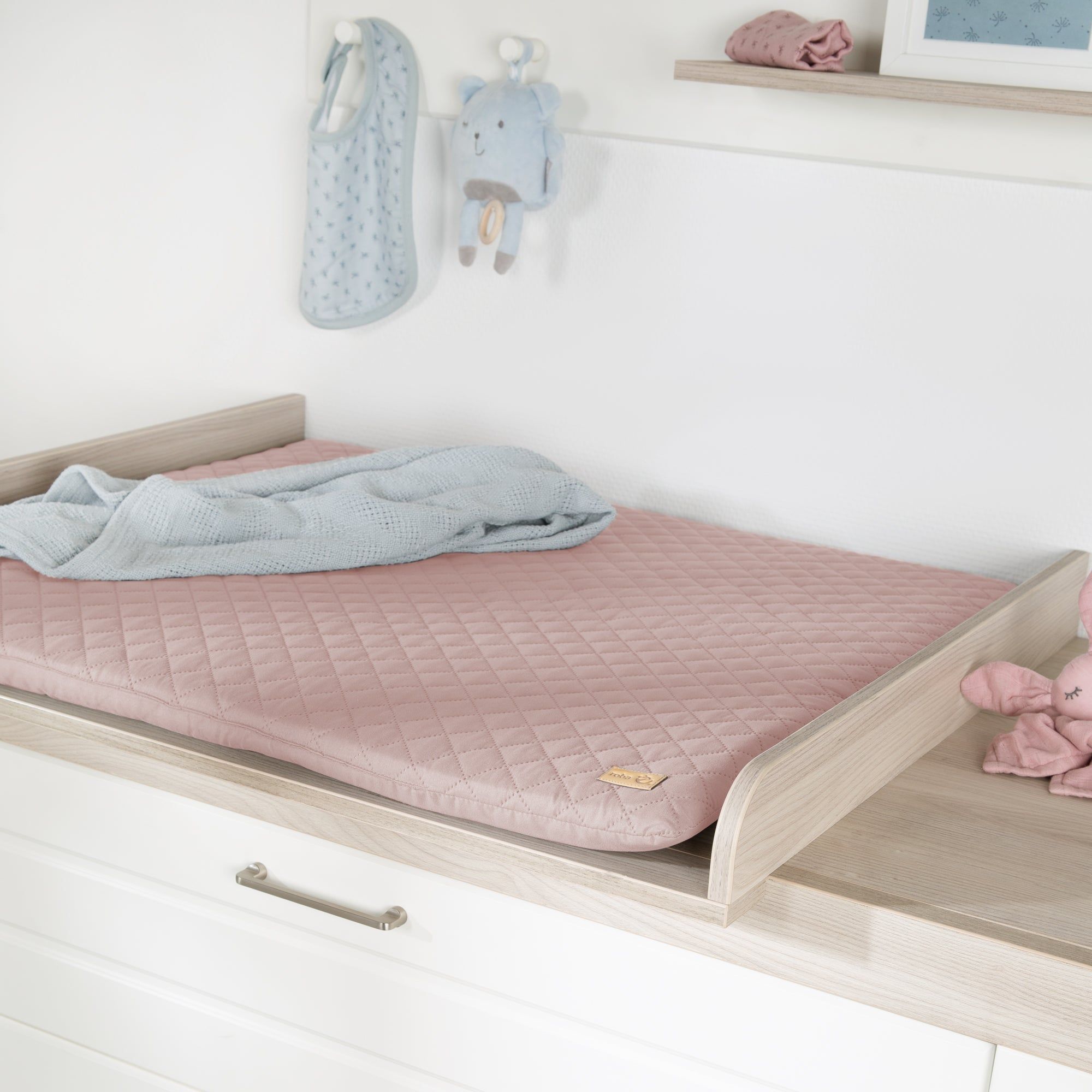 Rosa Wickelauflage auf Wickeltisch. Steppmuster. Label. Baby-Accessoires im Hintergrund.