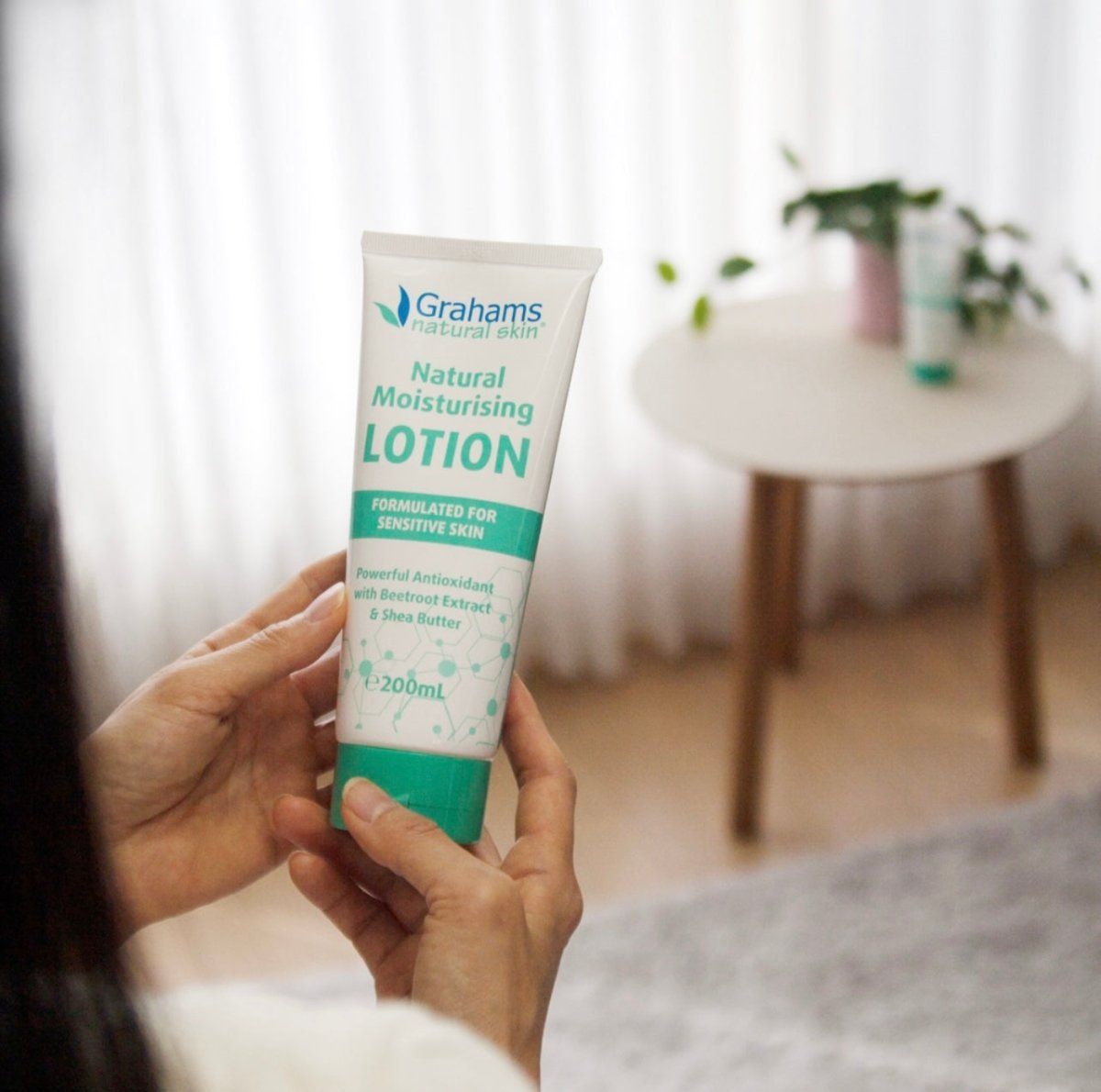 Person hält Tube. Grahams Natural Skin Natural Moisturising Lotion. Formulierung für empfindliche Haut. 200ml.