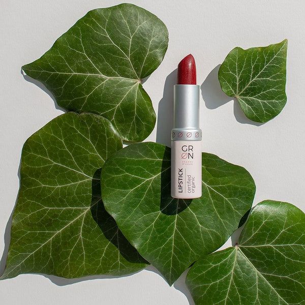 Lippenstift mit roter Spitze, umgeben von grünen Blättern. Silberne Hülse mit Schriftzug GRN und 'certified organic'.