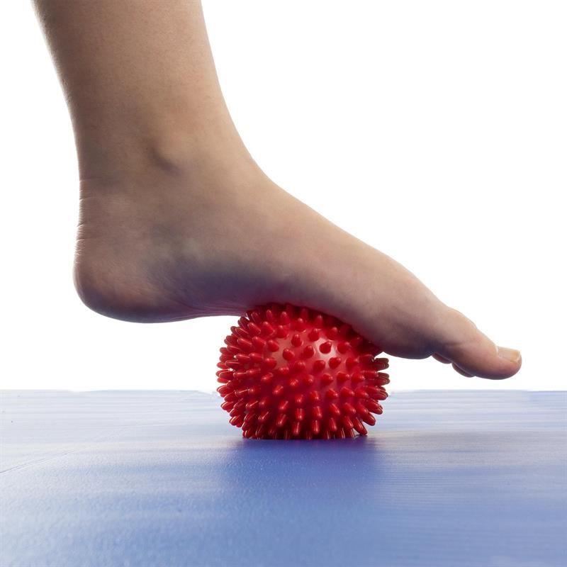 Roter Massageball mit Noppen unter Fuß. Auf blauem Untergrund.