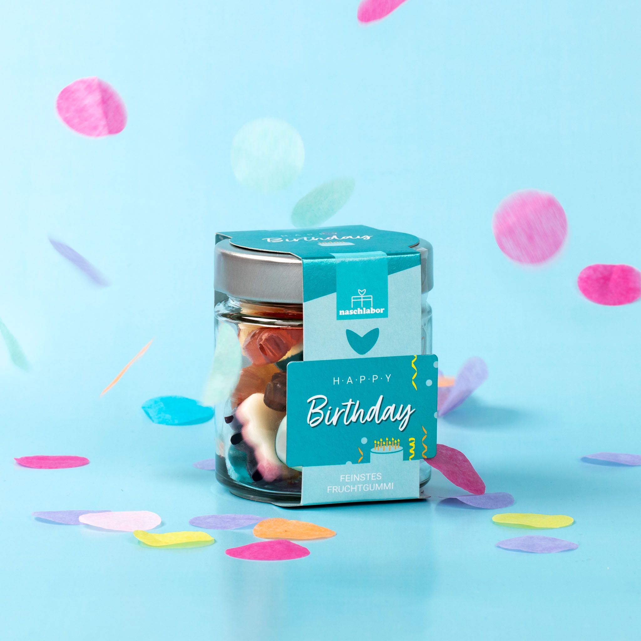 Glas mit Fruchtgummi, Label "Happy Birthday" und "naschlabor". Konfetti im Hintergrund. Verschiedene Fruchtgummi-Formen und -Farben.