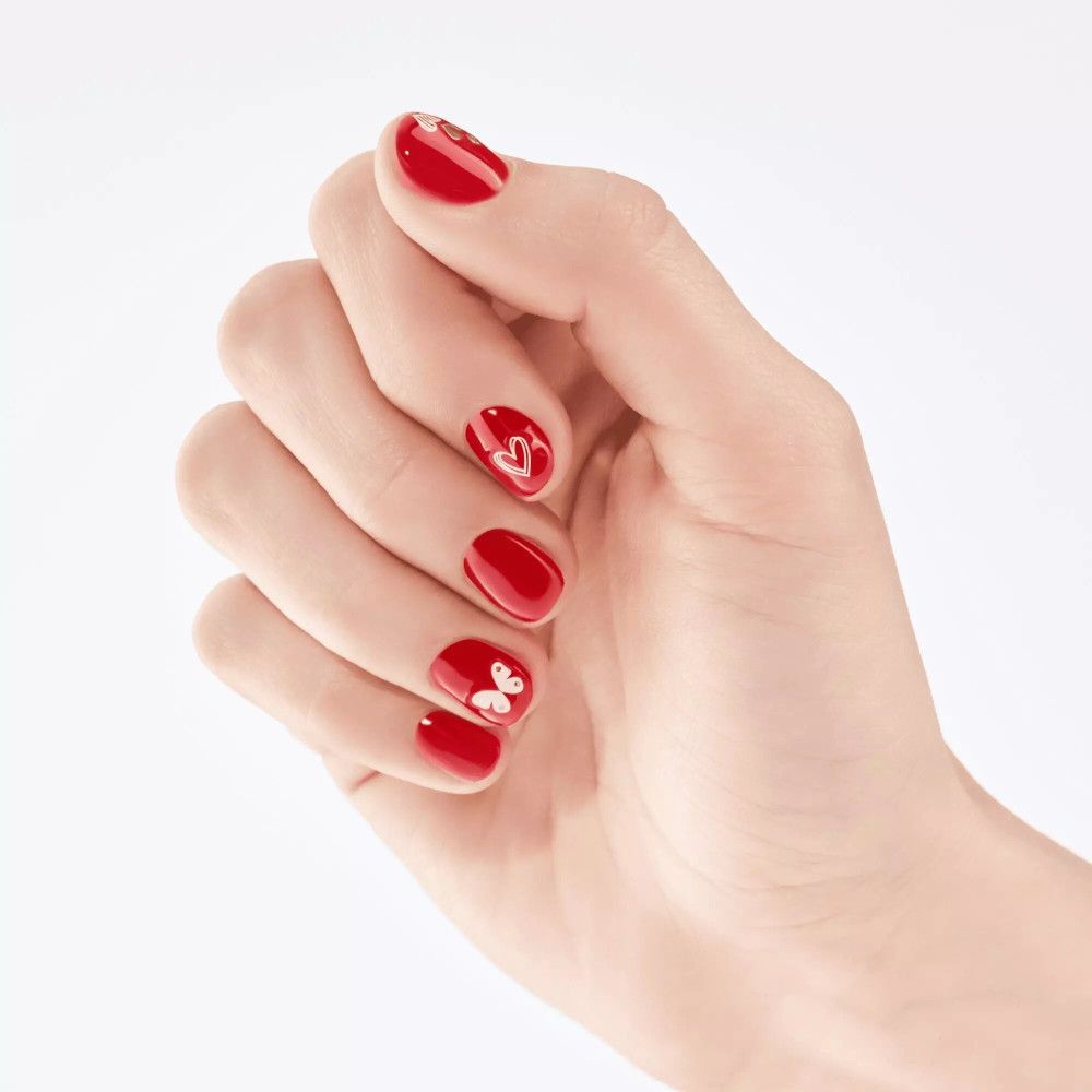 Hand mit roten, lackierten Nägeln. Einige Nägel mit weißen Nagelstickern: Herz und Schmetterling.