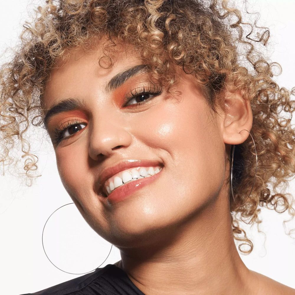 Frau mit lockigem Haar und Lippenstift. Sie lächelt. Lippen glänzend.