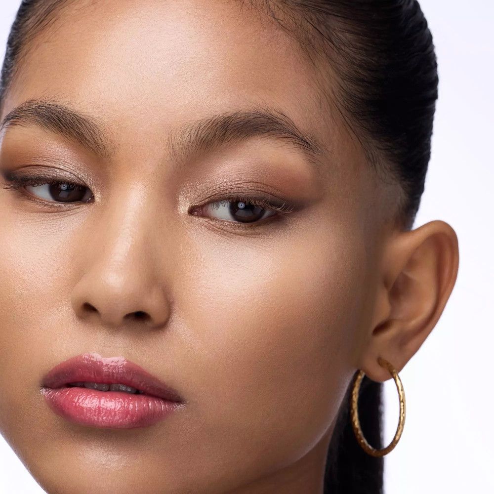 Nahaufnahme einer Frau mit goldfarbenen Creolen. Aufgetragenes Augen-Make-up.