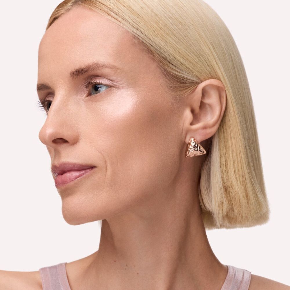 Porträt einer Frau mit blonden Haaren und aufgetragenem Highlighter auf den Wangenknochen. Goldene Ohrringe.