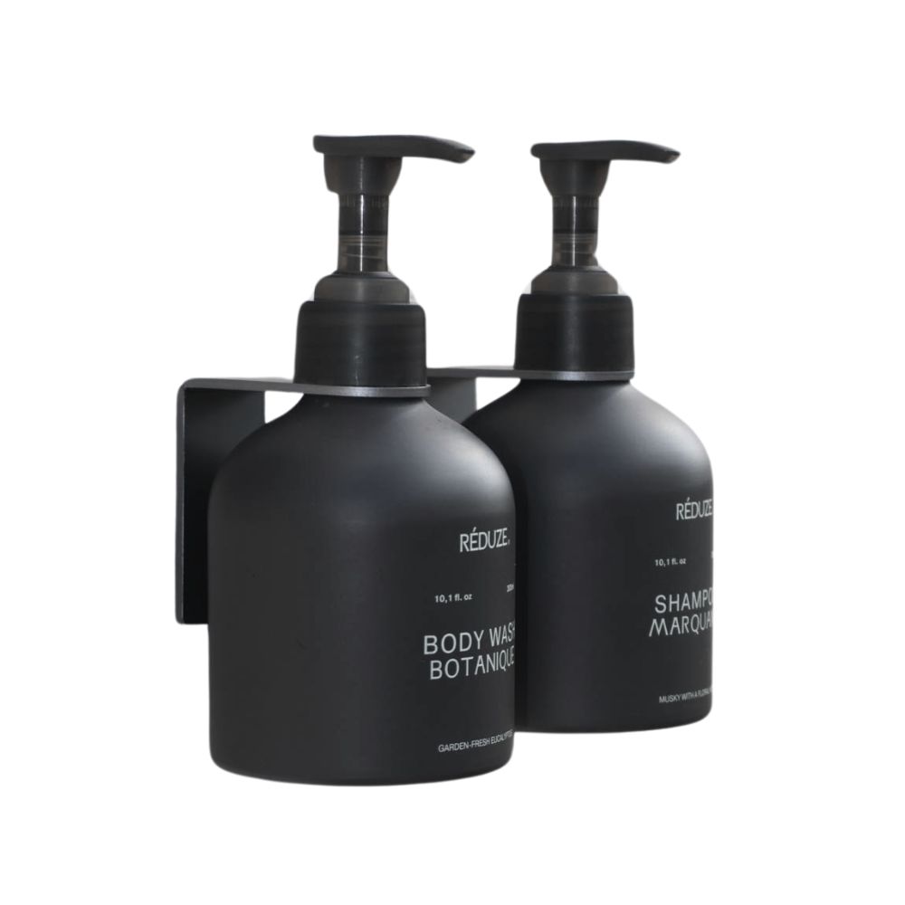 Zwei schwarze Flaschen mit Wandhalterungen. Aufschrift: RÉDUZE, Body Wash Botanique, Shampoo Marquant.