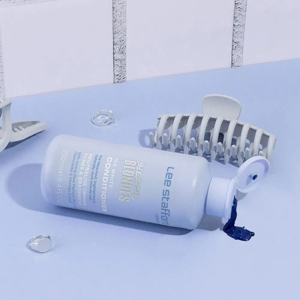 Hellblaue Flasche liegt. Daneben Haarklammern und durchsichtige Accessoires. Produkt: LEE STAFFORD Bleach Blondes Conditioner.