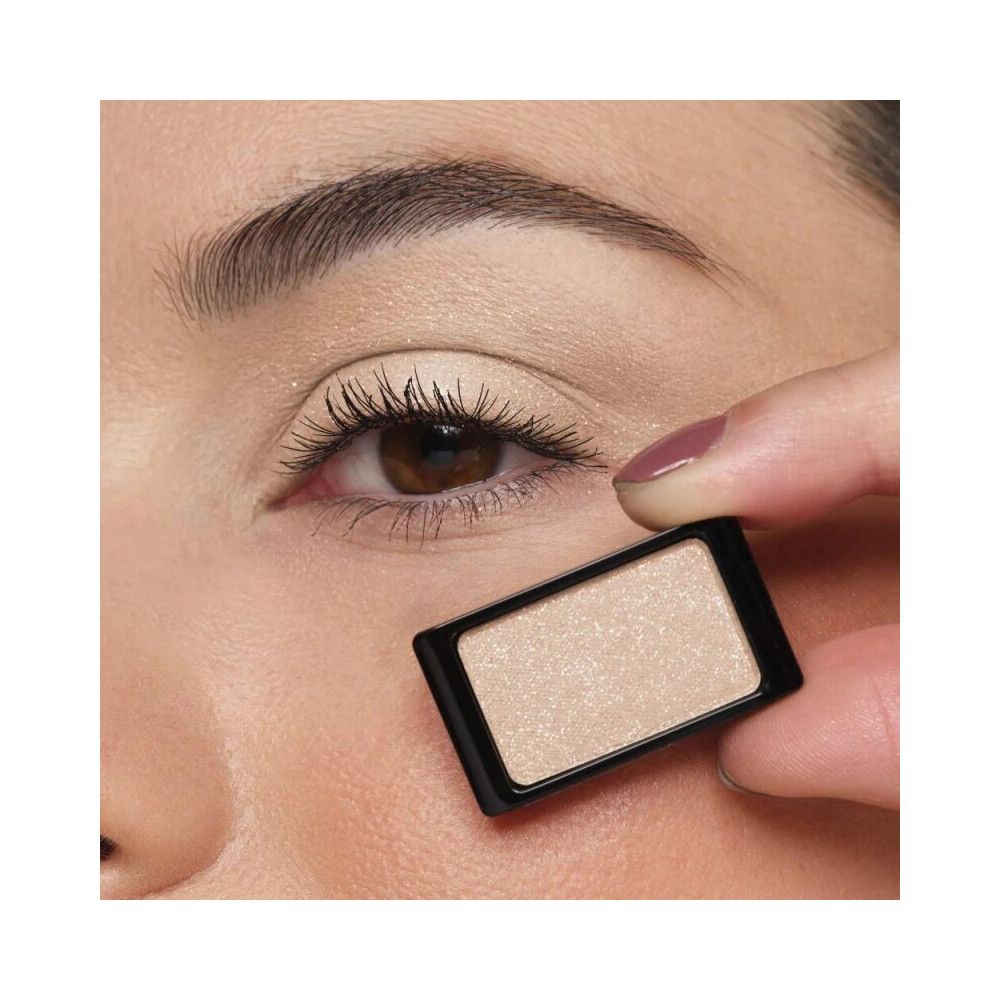 Auge mit Lidschatten. Ein rechteckiger, beiger Lidschatten wird vor dem Auge gehalten. Schwarzer Rahmen.