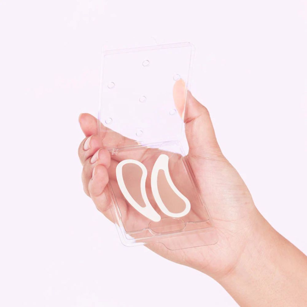 Hand hält transparente Kunststoffverpackung mit zwei NEEDLY Eye Patches. Patches in Hautfarbe.