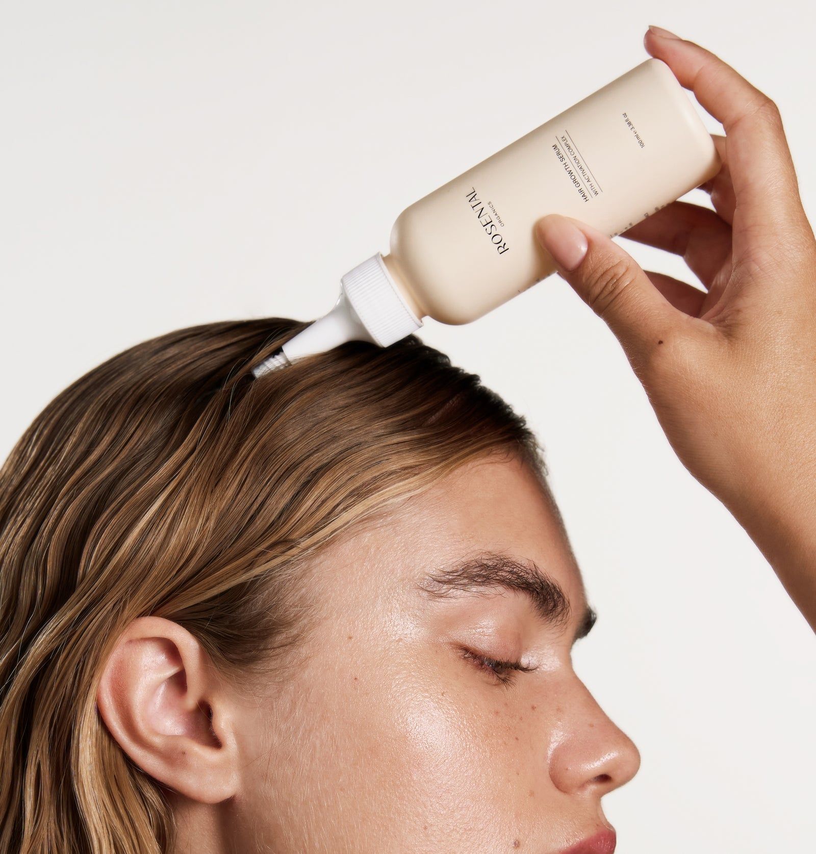 Person hält eine beige Flasche mit weißem Applikator über den Kopf einer Person. Produktname sichtbar.