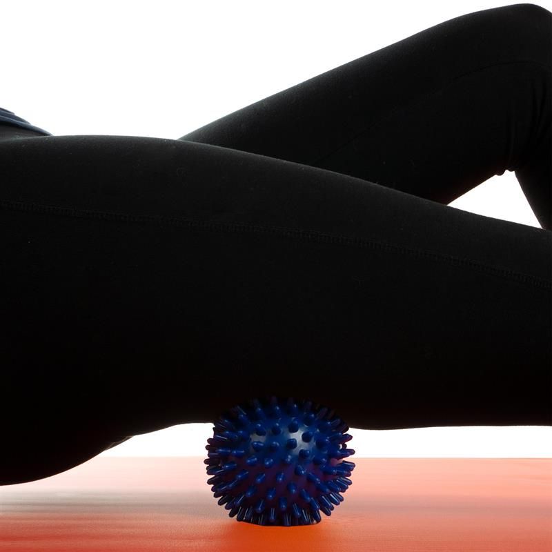 Person liegt mit dem Oberschenkel auf einer roten Matte. Darunter ein blauer Massageball.