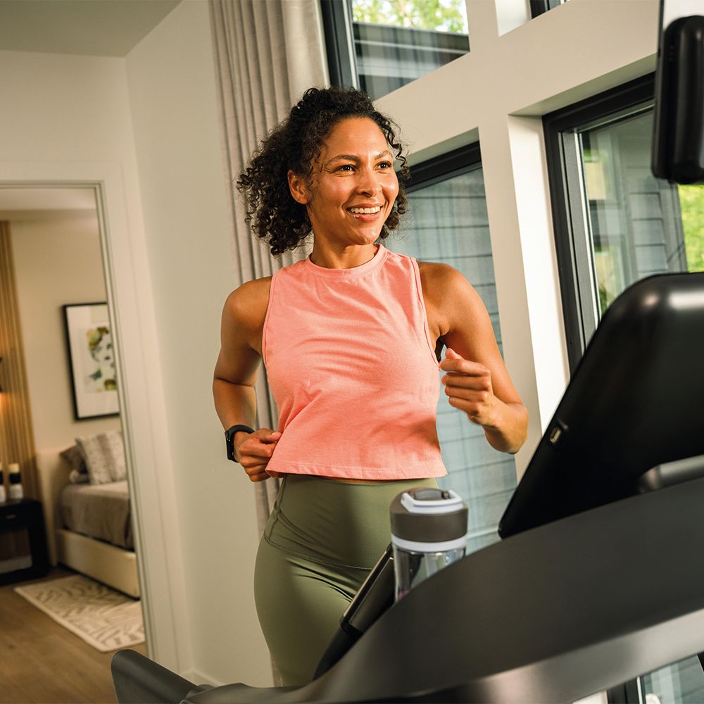 Frau läuft auf einem Laufband. Sie trägt Sportkleidung und hält eine Wasserflasche.