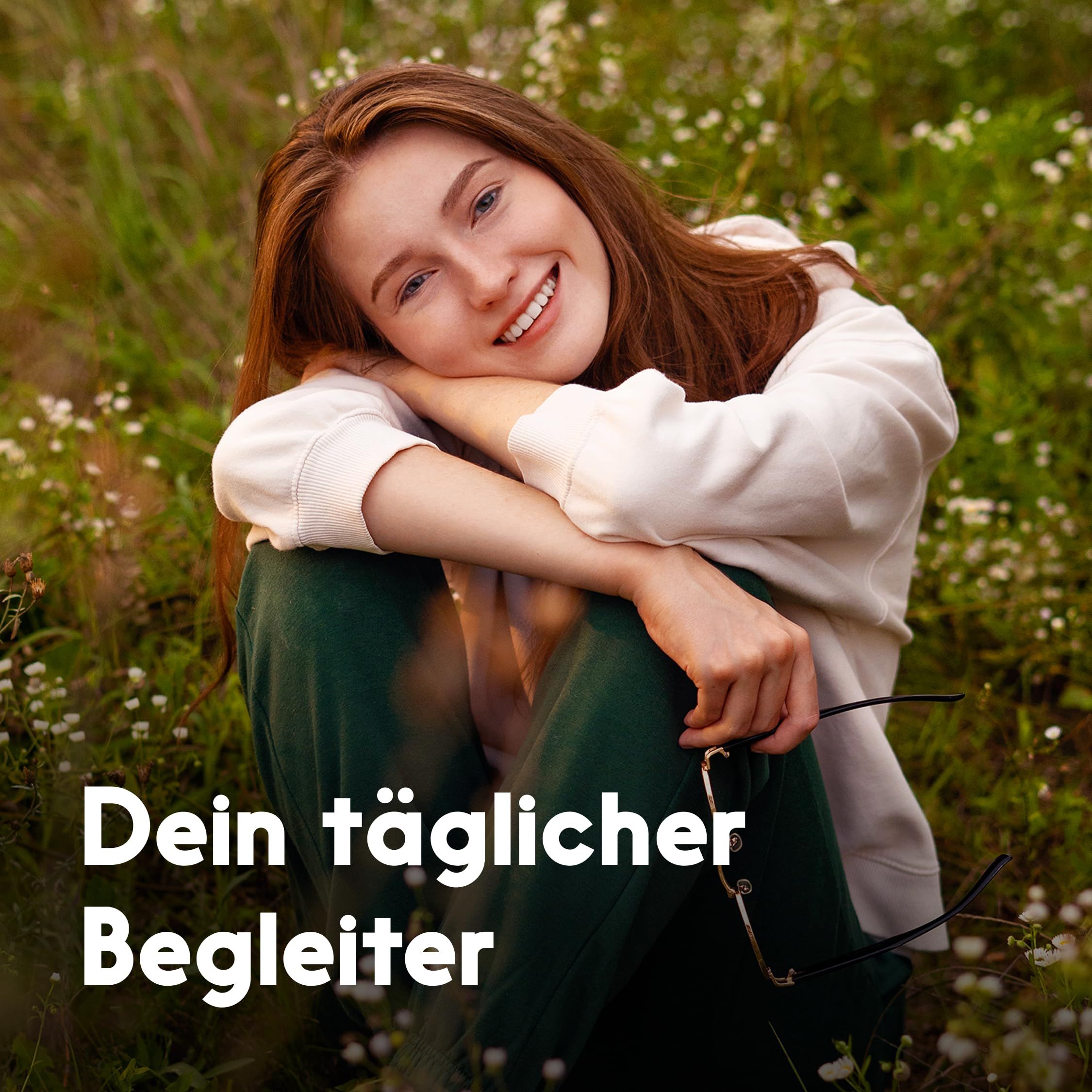 Junge Frau sitzt lächelnd in Blumenwiese. Text: "Dein täglicher Begleiter".