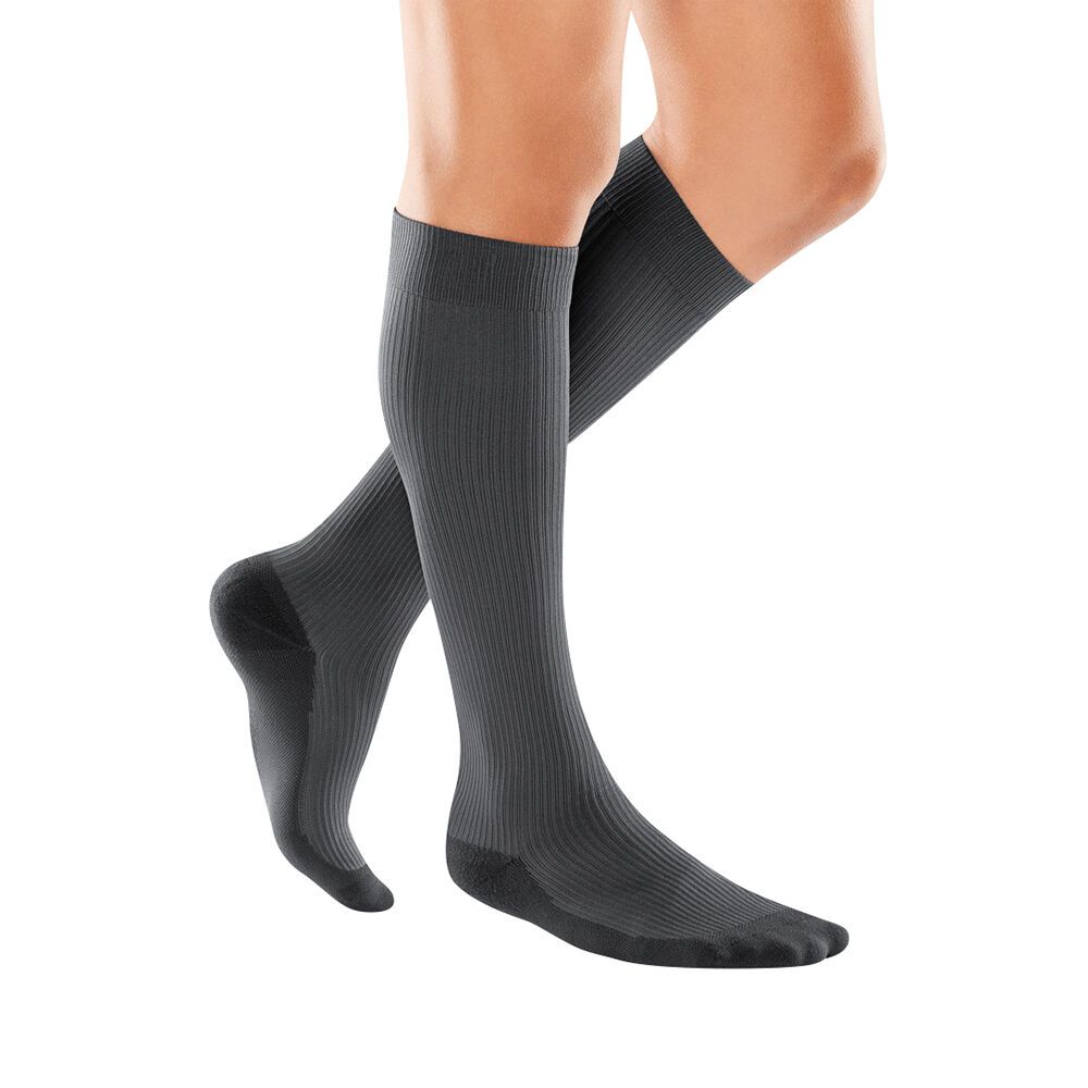 Zwei Beine mit grauen Kompressionsstrümpfen. Die Strümpfe sind gerippt und reichen bis zum Knie. Schwarze Fußspitze.