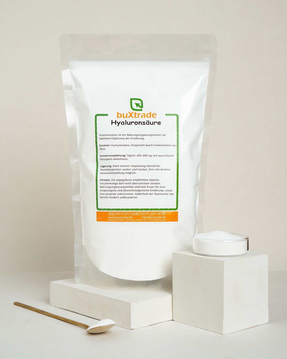 Verpackung von buXtrade Hyaluronsäure neben einem Würfel und einem Löffel.