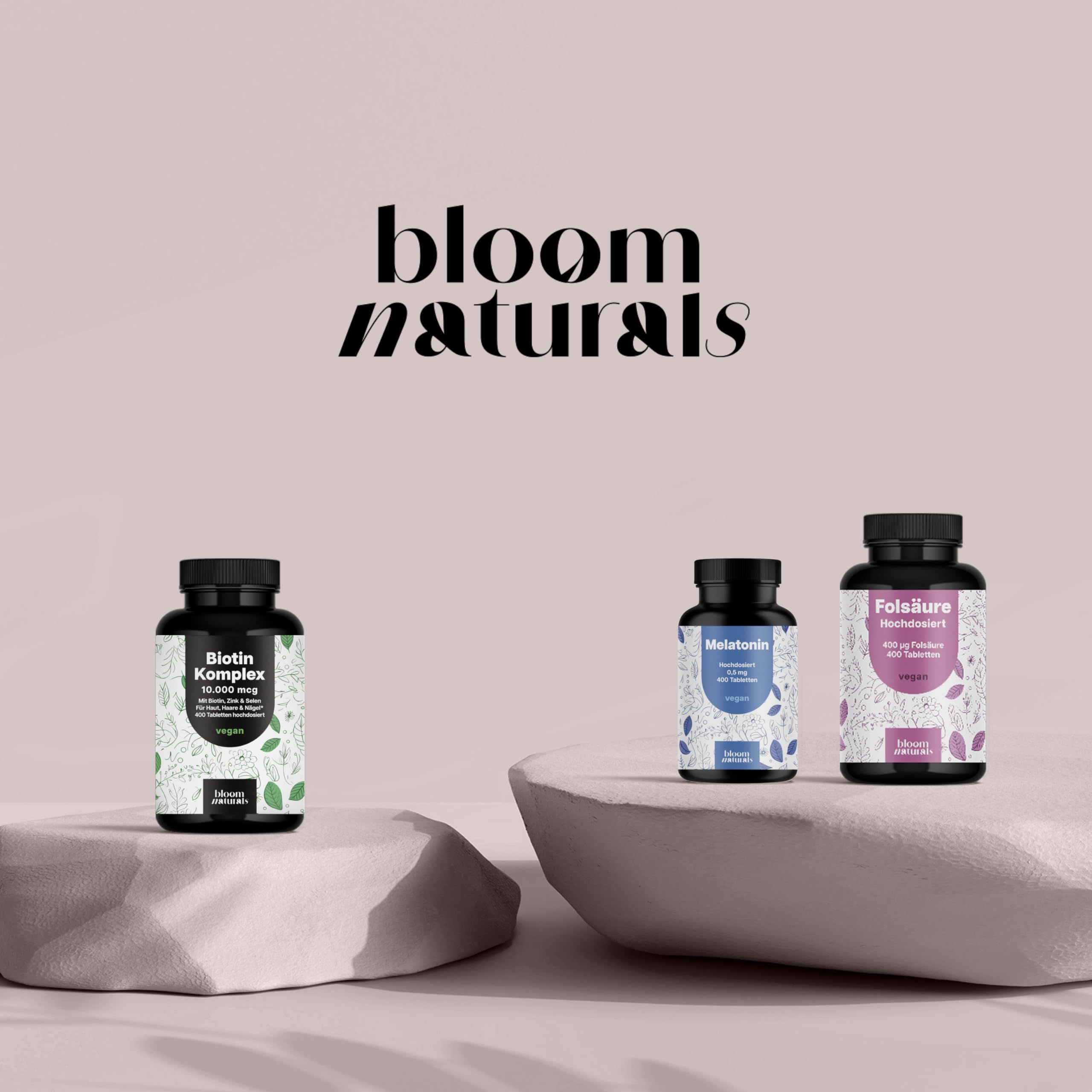 Drei Bloom Naturals Flaschen: Biotin Komplex, Melatonin, Folsäure, auf Steinen arrangiert.