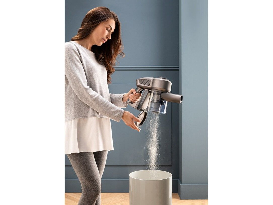 Frau entleert einen Handstaubsauger in einen Mülleimer. Der Staubsauger ist silberfarben.