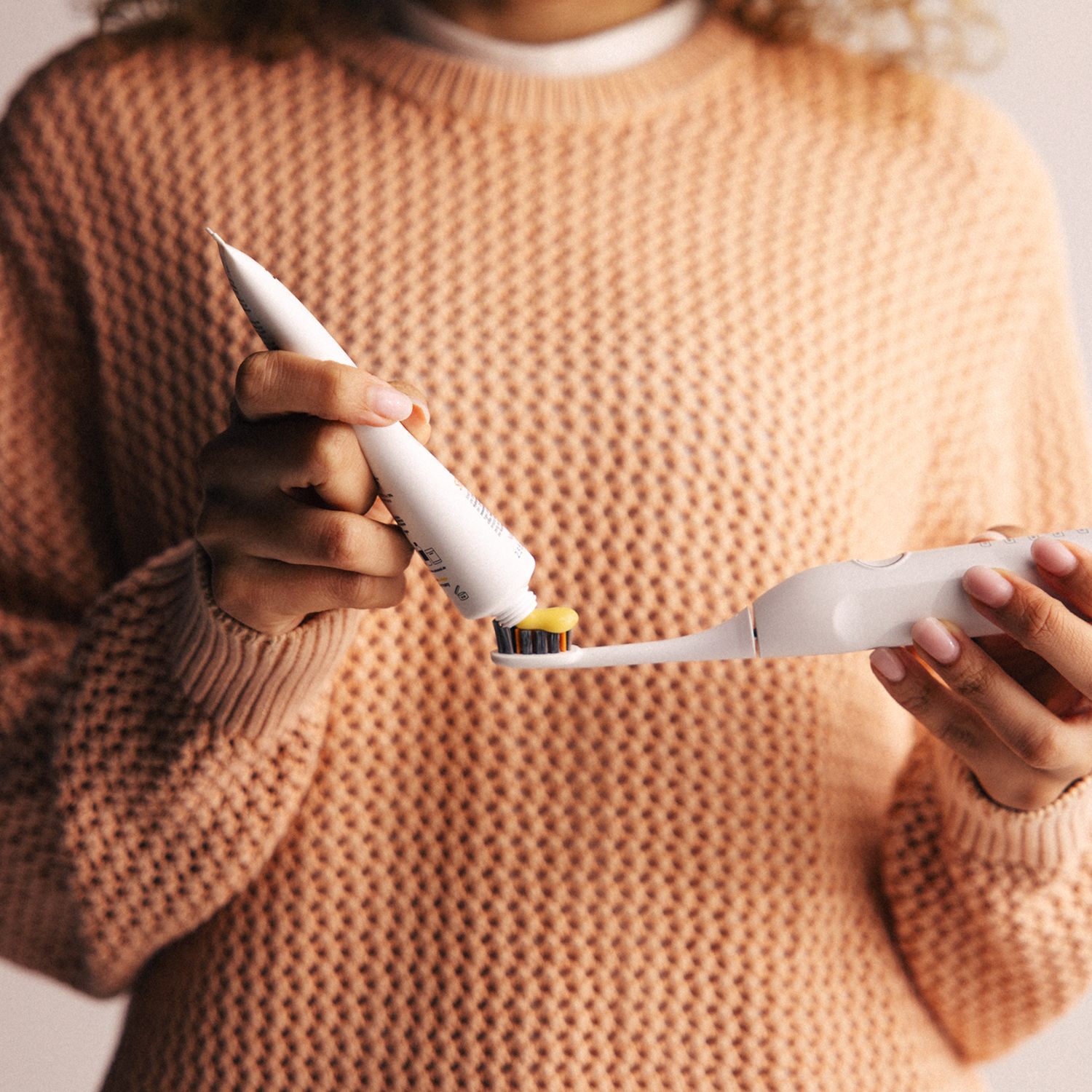 Person presst Zahnpasta auf eine elektrische Zahnbürste. Tube mit Aufschrift Zahnheld Sensitive.