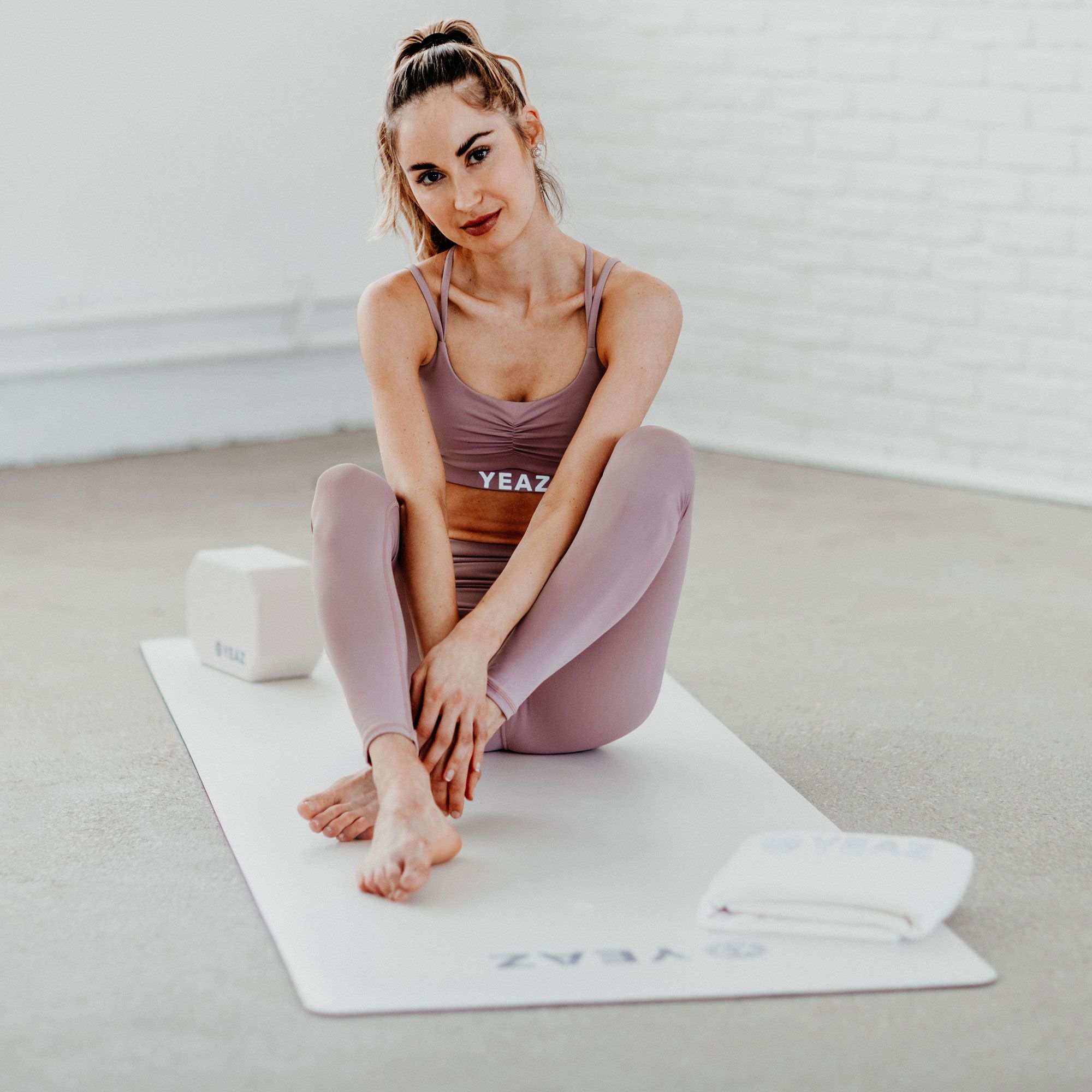 Frau sitzt auf Yogamatte. Matte, Handtuch und Blöcke. Logo YEAZ sichtbar.